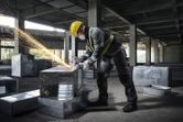 一名配戴安全設備的人員在建築工地上使用角磨機打磨金屬管路。.