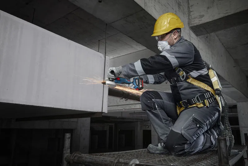 在建築工地上，一名配戴安全設備的工人正在用電動工具打磨混凝土。.