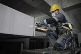 在建築工地上，一名配戴安全設備的工人正在用電動工具打磨混凝土。.