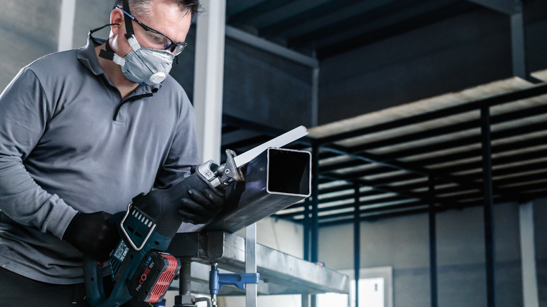 一名配戴安全設備的人員用往復鋸切割金屬管。