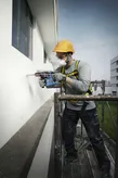 一名配戴安全設備的人員從鷹架上鑽入建築物牆壁。.