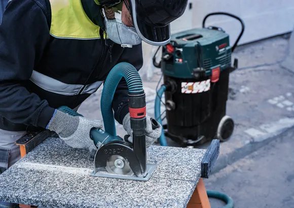 佩戴安全設備的人員使用連接到除塵器的圓鋸切割石頭。