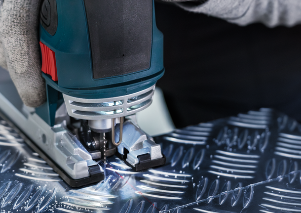 配戴安全設備的人使用曲線鋸切割有圖案的金屬。