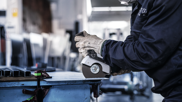 一名配戴安全設備的人使用角磨機切割金屬。