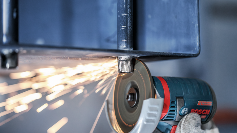 戴著手套、穿戴安全設備的工人用角磨機打磨金屬梁，產生火花。.