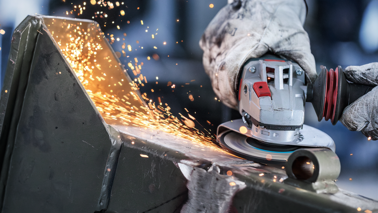 配戴安全設備的人員用角磨機研磨金屬，產生火花。