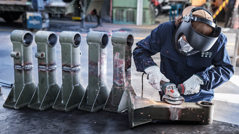 車間內，配戴安全設備的人員正在研磨金屬零件，產生火花。