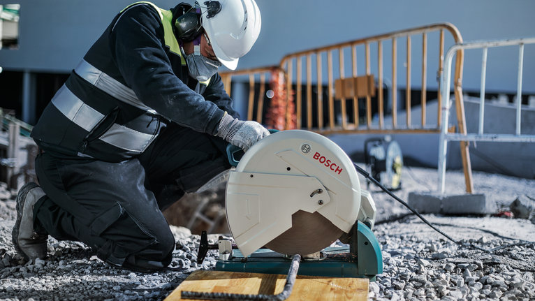在建築工地上，一名配戴安全設備的工人正在用切割鋸切割鋼筋。.