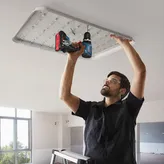 一名配戴安全設備的人員使用無線電鑽安裝天花板燈具。