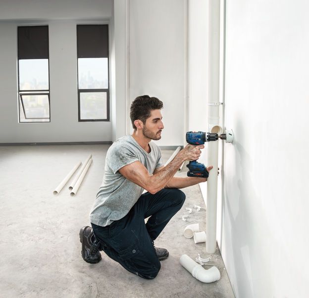 一個人在一間明亮的、未完工的房間裡鑽孔安裝管道。.