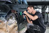 一名配戴安全設備的人員正在使用無線工具擦拭車門。.