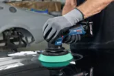 一名佩戴安全設備的人正在使用無線拋光機拋光汽車錶面。.