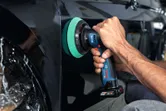 A person uses a cordless polisher on a car door.