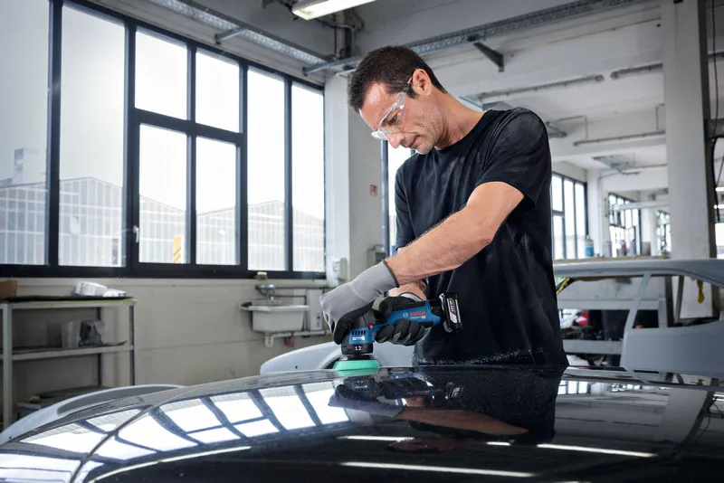 一名配戴安全設備的人員在汽車修理廠內擦拭汽車引擎蓋。.