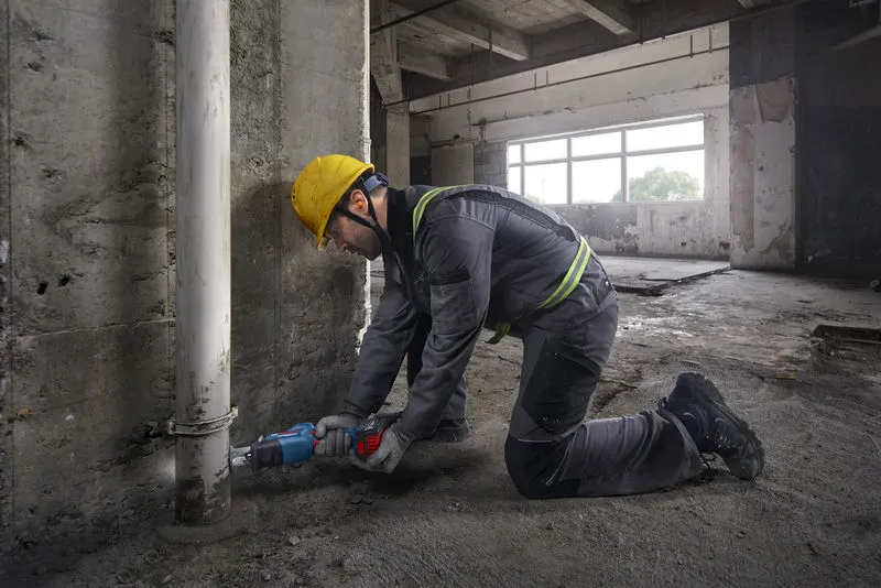 GSA 18V-24 一名配戴安全設備的人員使用往復鋸切割混凝土牆附近的管道。.