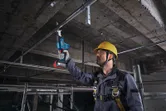 一名佩戴安全裝備的工人正在使用往復鋸切割天花板管道。