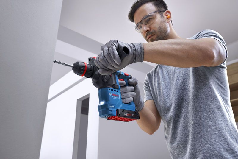 一名佩戴安全設備的人員使用無線旋轉錘在混凝土牆上鑽孔。.