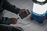 一名男子在水泥地面上使用無線工地燈為智慧型手機充電。.