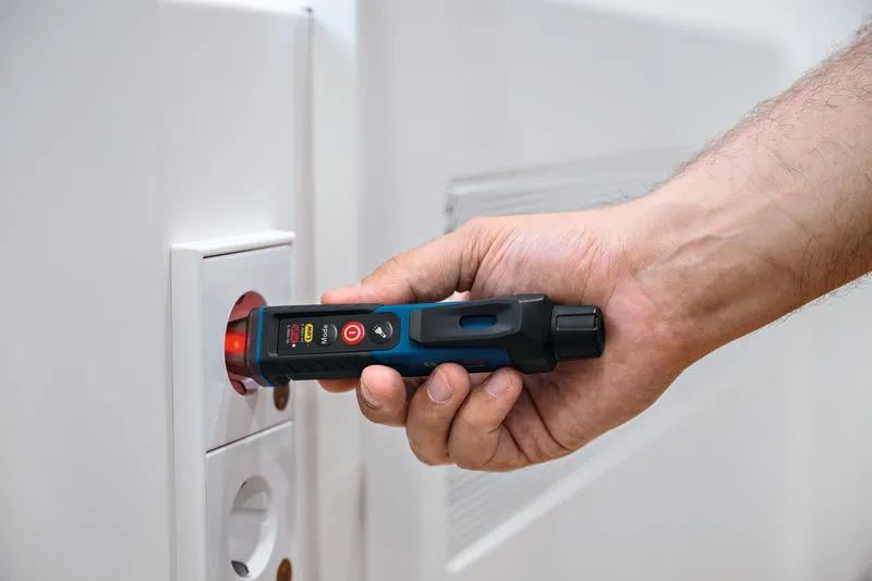 一個人在電源插座附近使用非接觸式電壓測試器。.