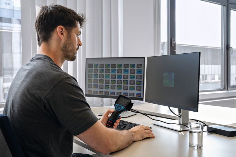 A person analyzes thermal images on dual monitors using a thermo camera at a desk.