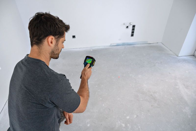 Person operates a thermo camera to inspect temperature variations on a bare floor.