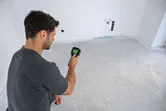 Person operates a thermo camera to inspect temperature variations on a bare floor.
