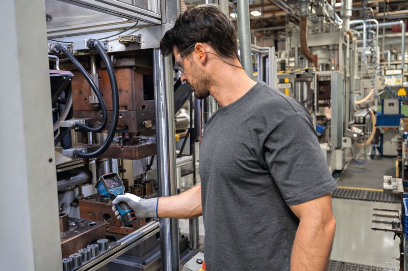 A person wearing safety equipment inspects machinery using a thermo camera.