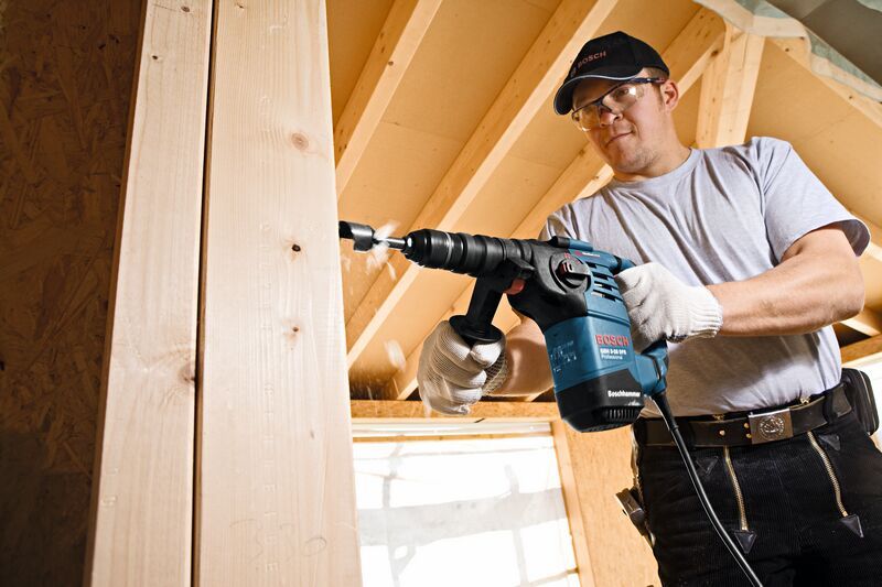 配戴安全設備的人員使用旋轉錘在木樑上鑽孔。.