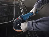 一名佩戴安全設備的人員正在使用電動拋光機拋光汽車車頂。.