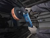 一名配戴安全設備的人員正在使用電動拋光機拋光車門。.
