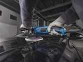 一名佩戴安全設備的人正在用藍色拋光機擦拭汽車引擎蓋。