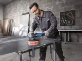 一名佩戴安全設備的人正在用電動工具拋光金屬板。.