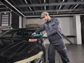 一名配戴安全設備的人員正在使用電動工具擦拭汽車引擎蓋。.