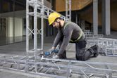 一名穿戴安全裝備的人員使用電動工具固定金屬框架結構。