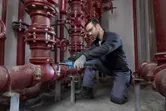 在工業環境中，一名穿戴安全裝備的人員正在使用電動工具擰緊管道接頭。
