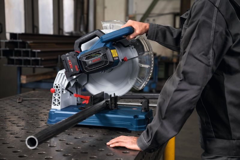 A person wearing safety equipment operates a metal cut-off saw cutting a pipe.