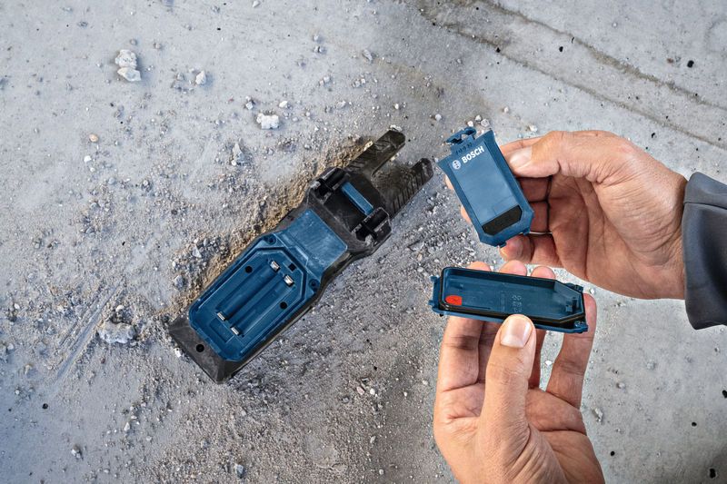 一名工人在佈滿灰塵的水泥地板上更換電動工具底座中的電池。.