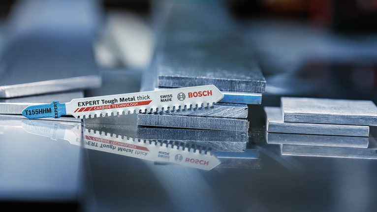 超耐久超厚金屬專業款 T155HHM 線鋸片,3 件 拼圖鋸刀片放置在反射表面上的堆疊金屬板上。