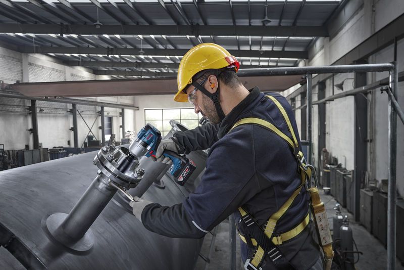 一名穿戴安全裝備的人員使用電動工具來擰緊工業管道上的螺栓。
