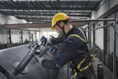 一名穿戴安全裝備的人員使用電動工具來擰緊工業管道上的螺栓。
