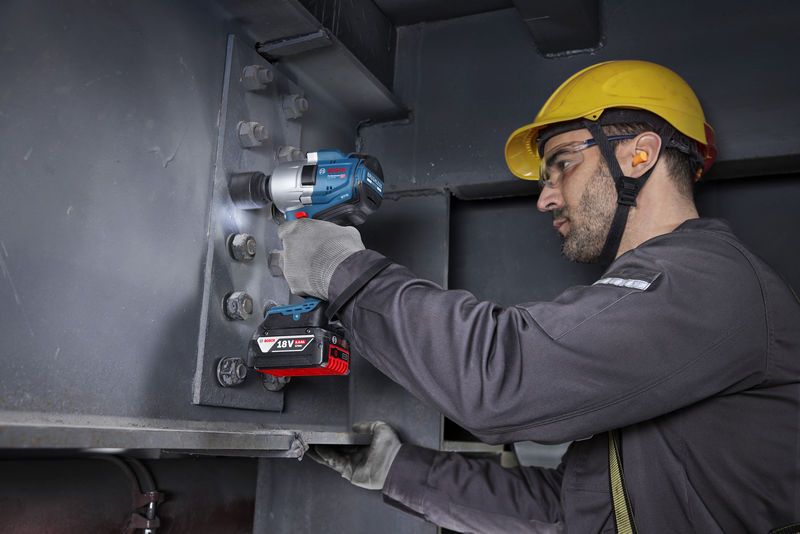 一名穿戴安全裝備的人員使用無線衝擊扳手來擰緊鋼樑上的螺栓。