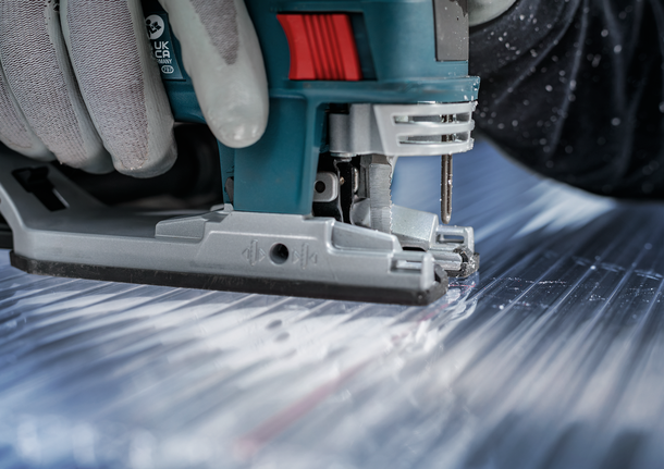 配戴安全設備的人員用曲線鋸切割金屬板。.