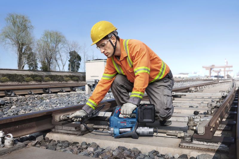 一名佩戴安全設備的人員使用無線黃油槍維護鐵軌。.
