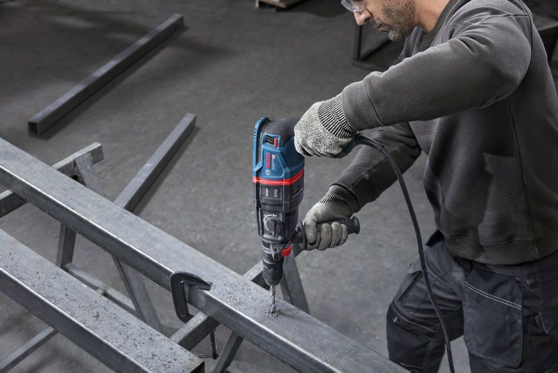 一名配戴安全設備的人員使用旋轉錘在金屬樑上鑽孔。.