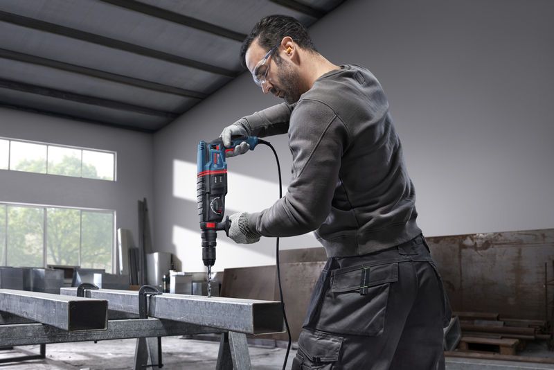 一名佩戴安全設備的人員使用旋轉錘在鋼樑上鑽孔。.