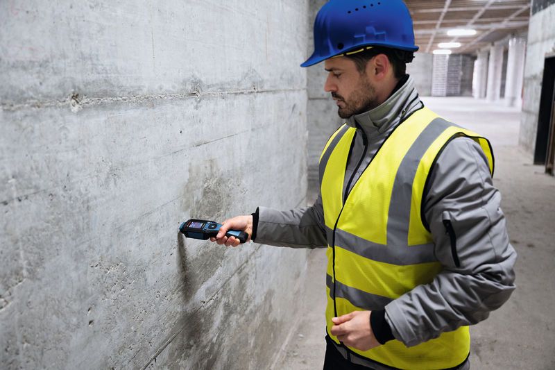 一名配戴安全設備的人員使用材料濕度計檢查混凝土牆體的濕度。.