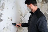 一名佩戴安全設備的人員使用材料濕度計對受損牆壁進行測量。.