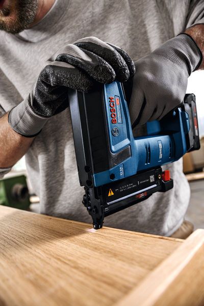 GNH 18V-35 一名佩戴安全設備的人使用無線釘槍在木質表面上工作。.