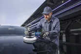 一名佩戴安全設備的人正在用電動拋光機拋光一輛黑色汽車。.