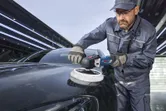 一名配戴安全設備的人員正在使用電動拋光機拋光黑色汽車引擎蓋。.